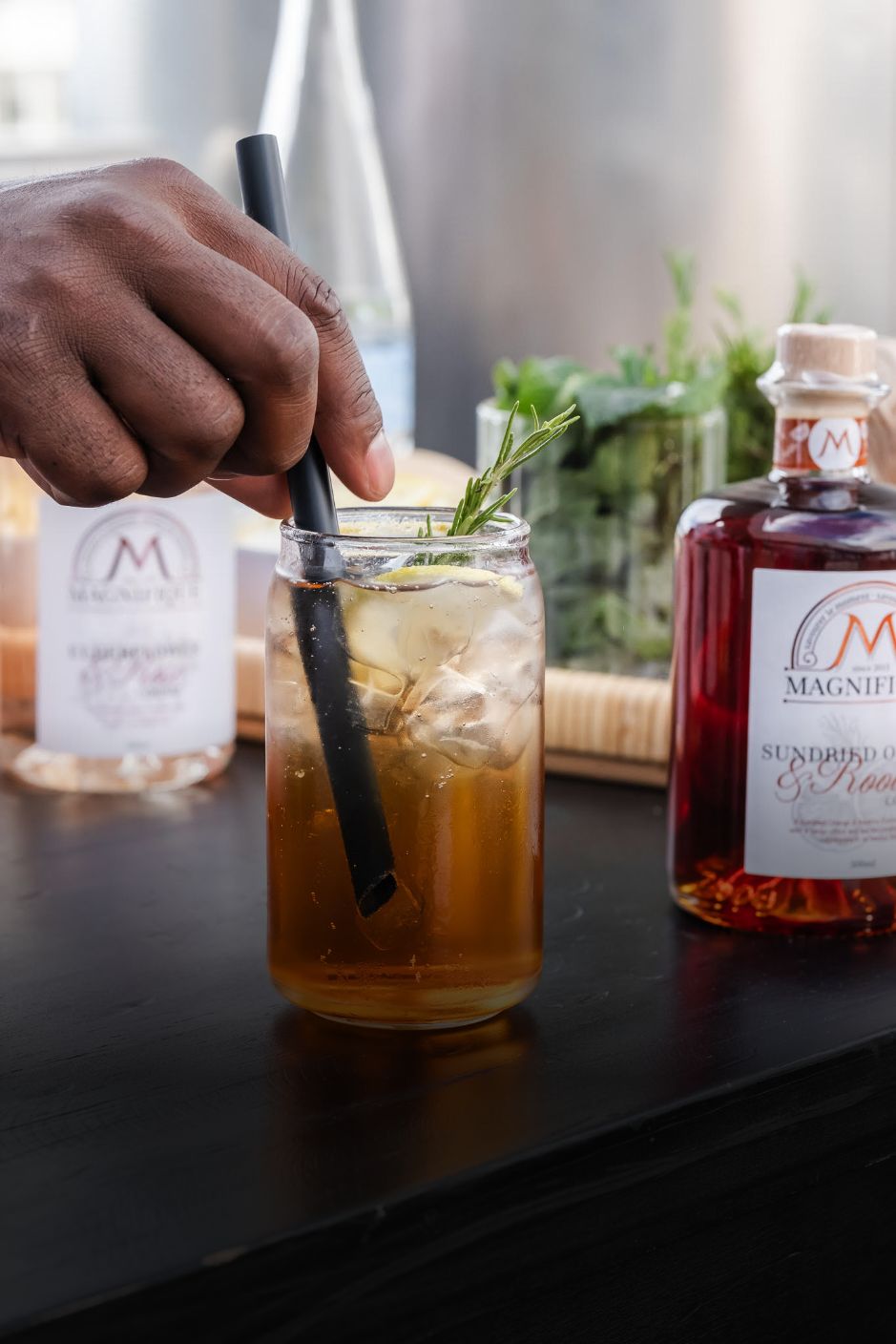 Barista stirring a Magnifique cordial and tonic over ice at a bar.